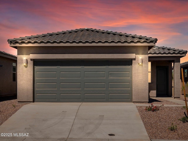 mediterranean / spanish-style home with an attached garage, stucco siding, a tile roof, and concrete driveway