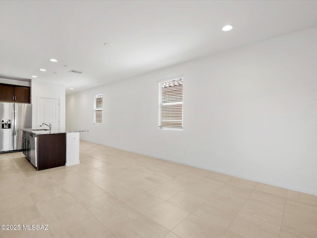 kitchen with recessed lighting, dark brown cabinetry, light stone countertops, and stainless steel fridge with ice dispenser