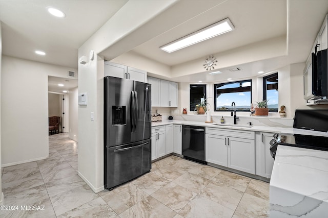 kitchen featuring black dishwasher, light stone counters, stainless steel fridge, and white cabinetry