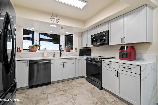 kitchen with black appliances, white cabinetry, a raised ceiling, and sink