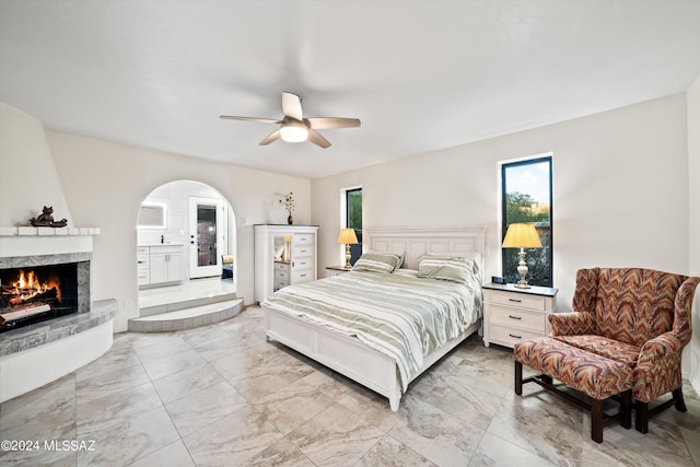 bedroom with arched walkways, marble finish floor, a fireplace, and ceiling fan