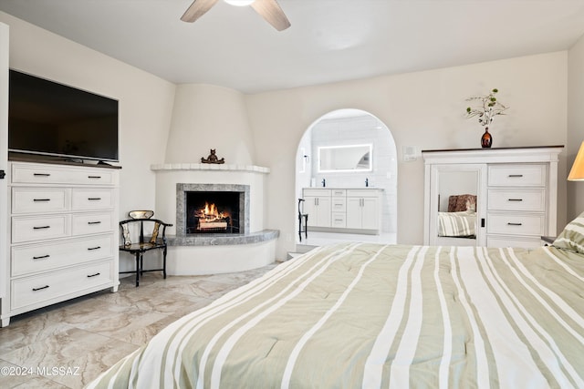 bedroom featuring a large fireplace, ceiling fan, and ensuite bathroom