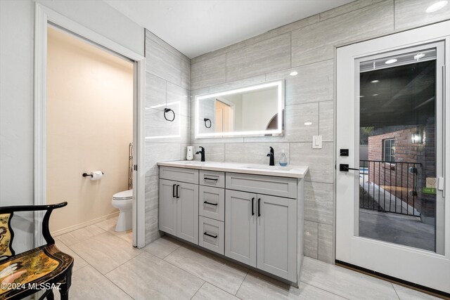 bathroom featuring double vanity, toilet, tile walls, and a sink