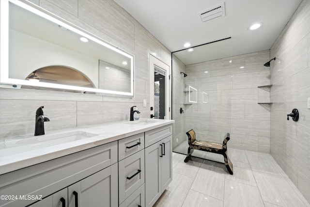 bathroom with tiled shower, vanity, and tile walls