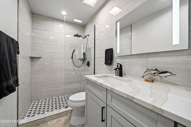 bathroom with toilet, tile walls, vanity, and a tile shower