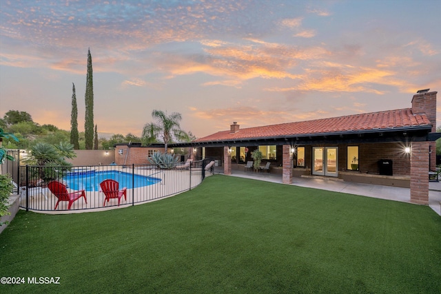 pool at dusk featuring a fenced in pool, fence, a yard, french doors, and a patio area