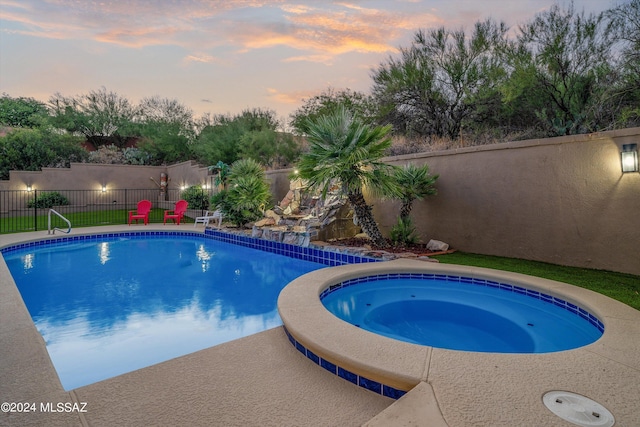 pool at dusk with an in ground hot tub and a patio area