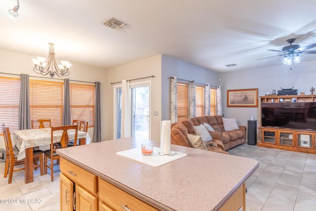 kitchen with hanging light fixtures, ceiling fan with notable chandelier, light brown cabinets, light tile patterned flooring, and a kitchen island