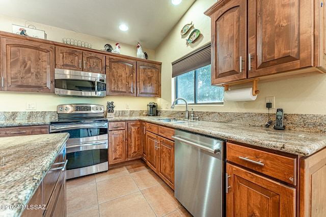 kitchen with appliances with stainless steel finishes, light stone countertops, light tile patterned flooring, and sink