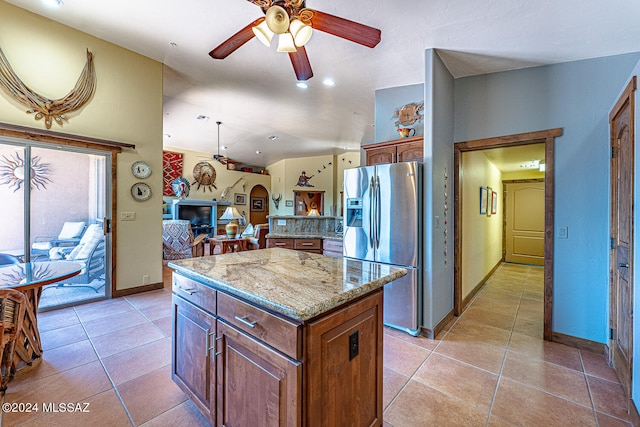 kitchen featuring a kitchen island, stainless steel refrigerator with ice dispenser, light tile patterned floors, ceiling fan, and light stone counters