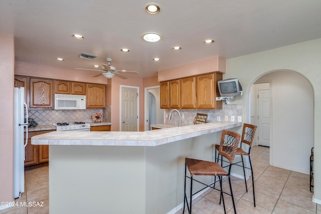 kitchen featuring backsplash, white appliances, kitchen peninsula, and a breakfast bar