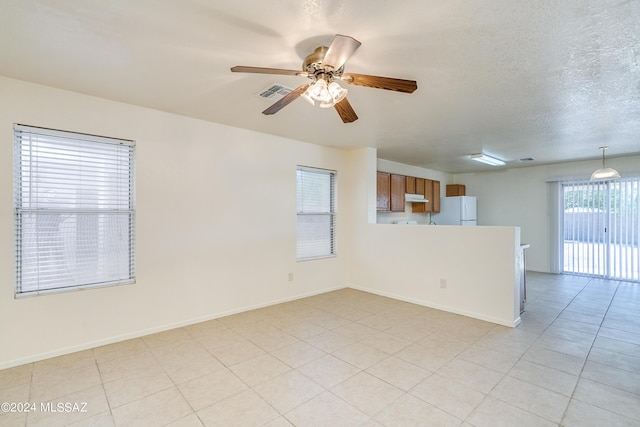 empty room featuring visible vents, a ceiling fan, a textured ceiling, light tile patterned floors, and baseboards