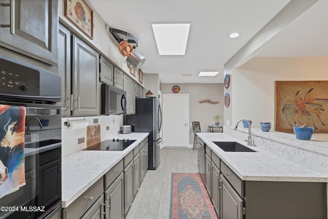 kitchen featuring light wood-type flooring, black appliances, light stone counters, and sink