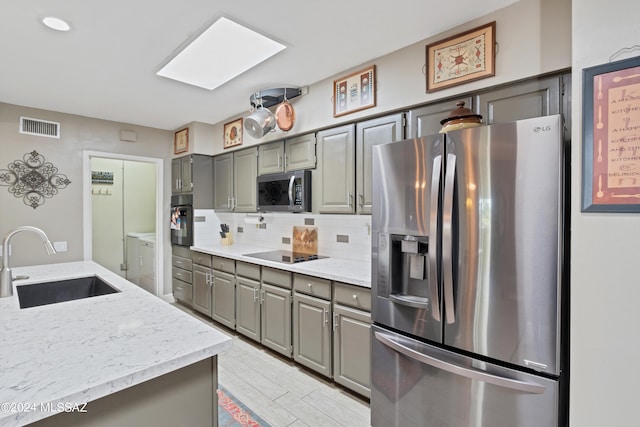 kitchen featuring black appliances, sink, decorative backsplash, a skylight, and washing machine and dryer