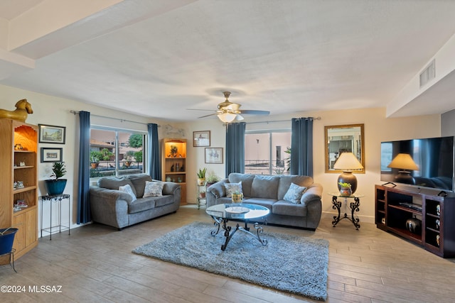 living room with hardwood / wood-style floors, visible vents, a ceiling fan, and baseboards