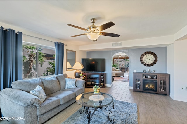 living area featuring arched walkways, a ceiling fan, wood finished floors, and visible vents