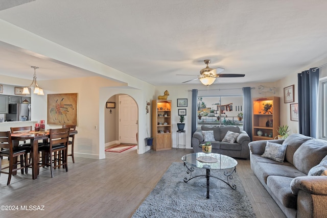 living area featuring baseboards, arched walkways, a ceiling fan, and light wood-type flooring