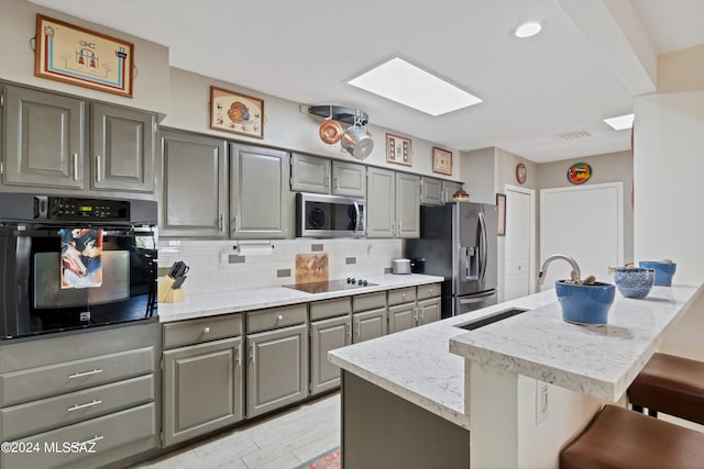 kitchen featuring light wood-type flooring, gray cabinets, tasteful backsplash, a kitchen breakfast bar, and black appliances