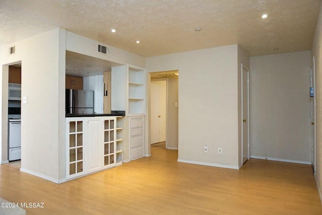 unfurnished living room featuring a textured ceiling, built in features, and light hardwood / wood-style floors