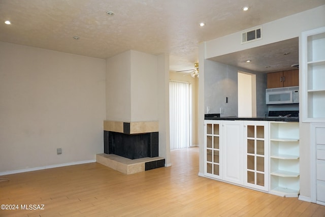 interior space with a textured ceiling, a tile fireplace, ceiling fan, and light wood-type flooring