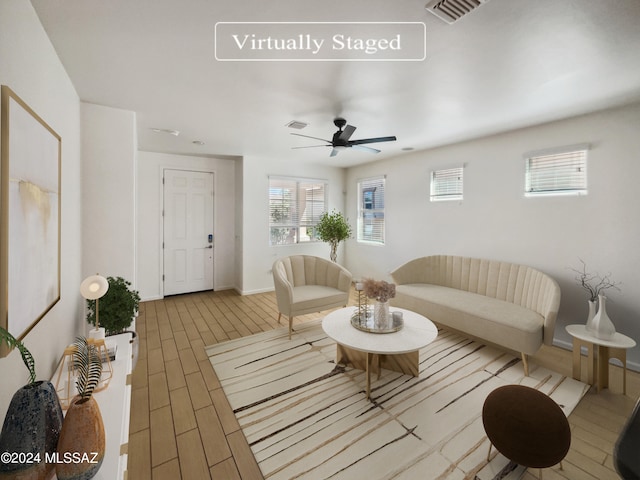 living area with baseboards, wood finished floors, visible vents, and ceiling fan