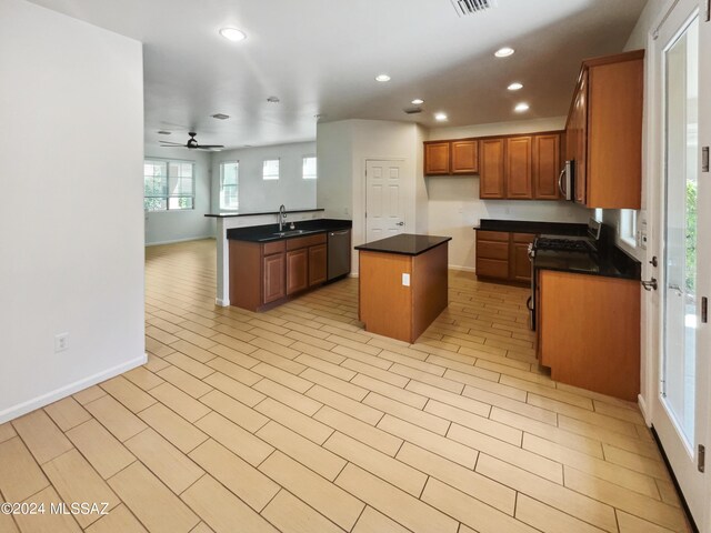 kitchen with dark countertops, a kitchen island, open floor plan, stainless steel appliances, and a sink