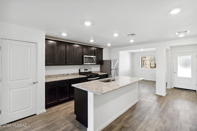 kitchen with light stone counters, stainless steel appliances, light hardwood / wood-style floors, sink, and a center island with sink