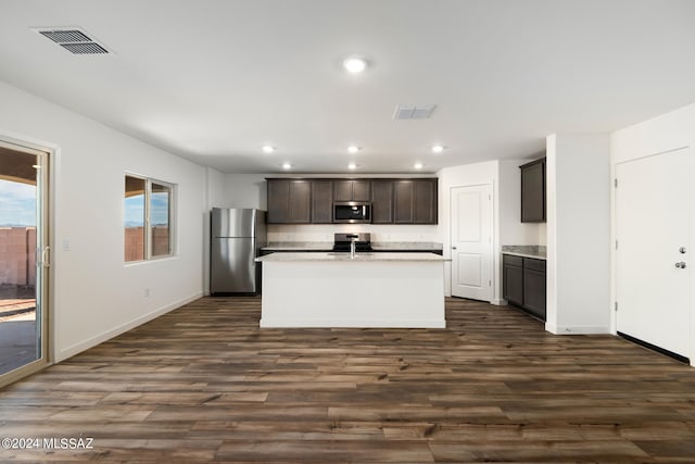 kitchen with an island with sink, dark wood-type flooring, appliances with stainless steel finishes, and dark brown cabinets