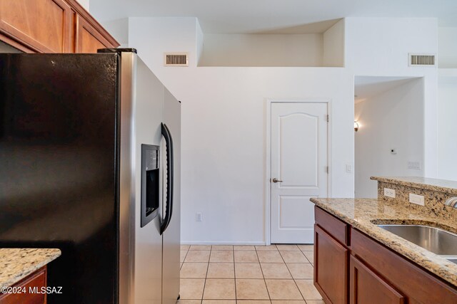 kitchen with light stone countertops, light tile patterned floors, stainless steel fridge with ice dispenser, and sink