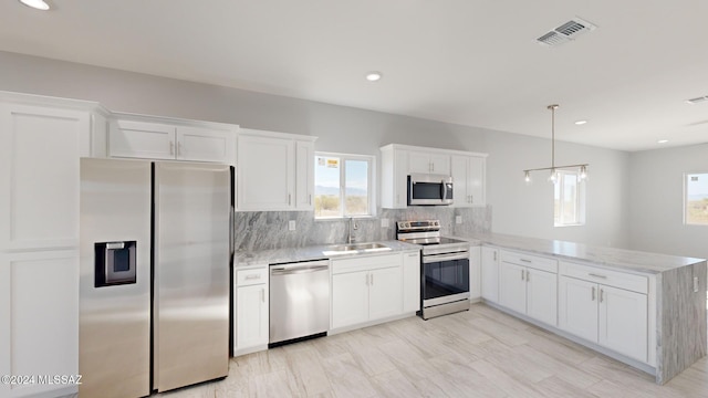 kitchen featuring kitchen peninsula, appliances with stainless steel finishes, sink, decorative light fixtures, and white cabinets