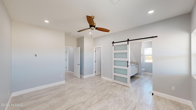 unfurnished bedroom featuring connected bathroom, a barn door, and ceiling fan