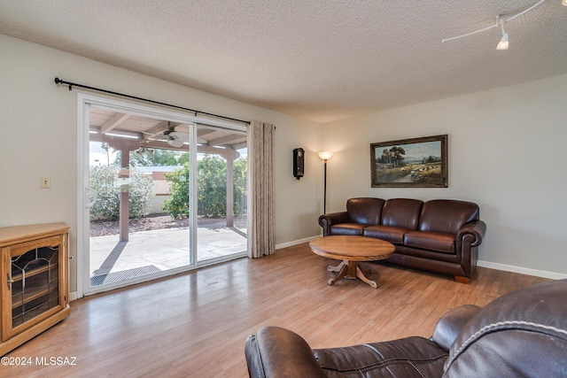 living room featuring ceiling fan, a textured ceiling, and light wood-type flooring