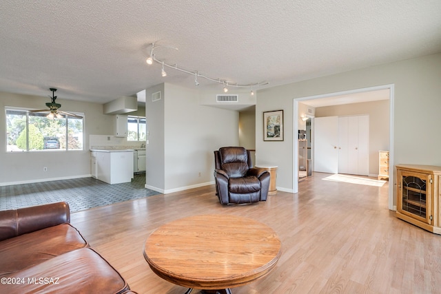 living room featuring ceiling fan, light wood-type flooring, a textured ceiling, and track lighting