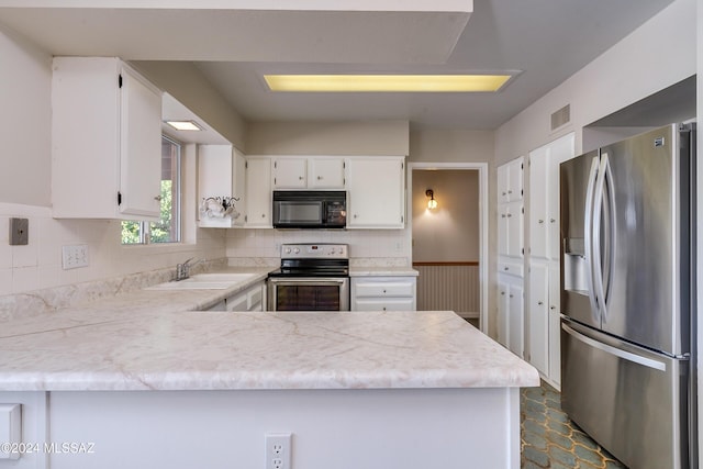 kitchen with kitchen peninsula, appliances with stainless steel finishes, tasteful backsplash, sink, and white cabinetry