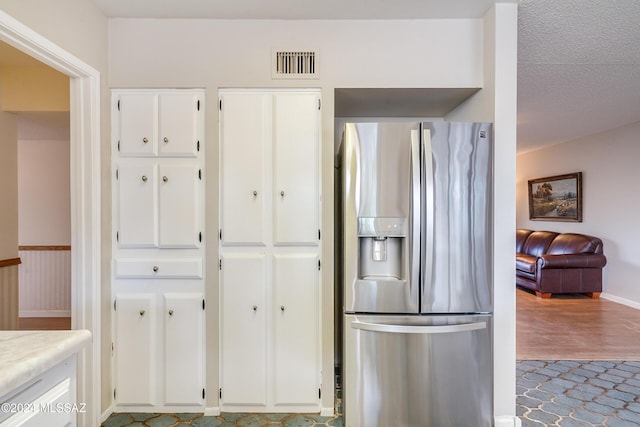 kitchen featuring white cabinets, stainless steel fridge, and a textured ceiling