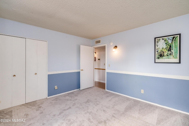 unfurnished bedroom with a textured ceiling, light colored carpet, and a closet