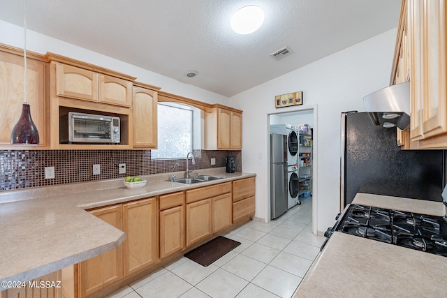 kitchen featuring lofted ceiling, stacked washing maching and dryer, light brown cabinetry, and sink