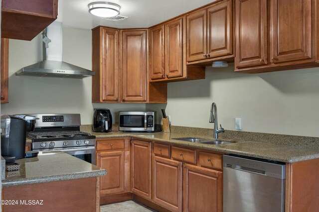 kitchen with light stone counters, stainless steel appliances, sink, and wall chimney range hood