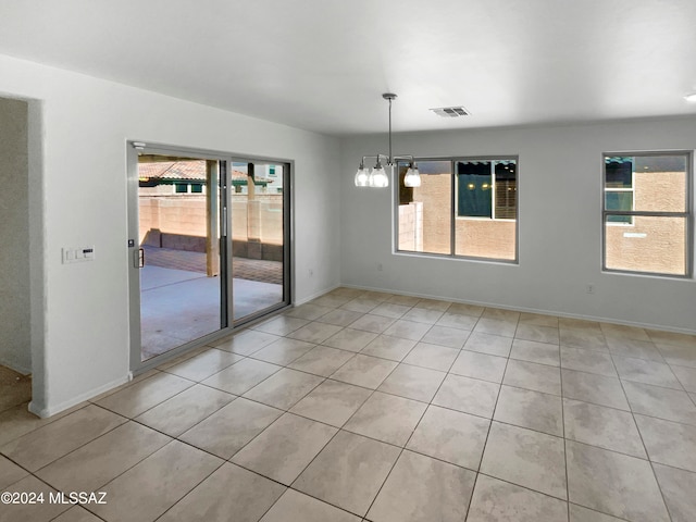 spare room featuring a wealth of natural light, an inviting chandelier, and light tile patterned flooring