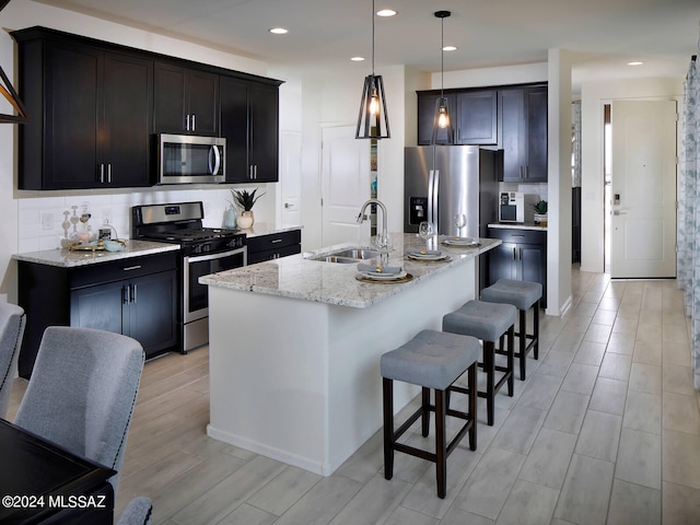 kitchen featuring pendant lighting, sink, an island with sink, appliances with stainless steel finishes, and light stone countertops