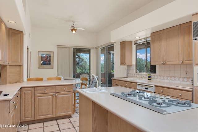 kitchen with backsplash, kitchen peninsula, white gas stovetop, and a healthy amount of sunlight