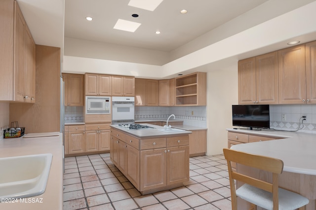 kitchen featuring decorative backsplash, white appliances, light brown cabinetry, a skylight, and sink