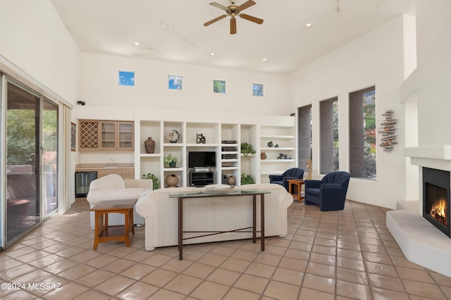 tiled living room with ceiling fan, wine cooler, a high ceiling, and built in shelves