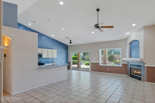 unfurnished living room featuring ceiling fan, light tile patterned flooring, sink, a tiled fireplace, and high vaulted ceiling