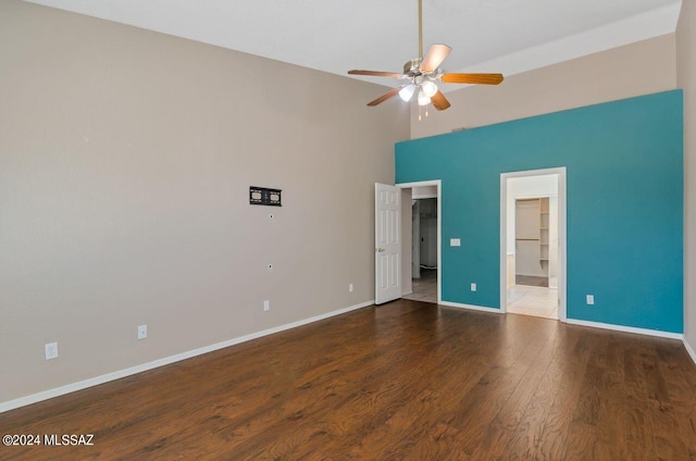 unfurnished bedroom featuring a ceiling fan, wood finished floors, baseboards, a high ceiling, and connected bathroom