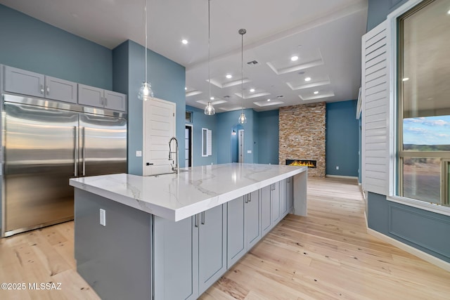 kitchen with a spacious island, light stone counters, gray cabinetry, and built in refrigerator