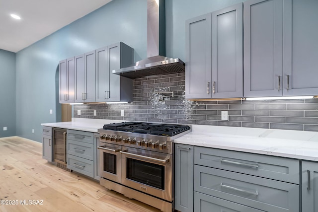 kitchen featuring double oven range, gray cabinetry, wall chimney exhaust hood, light stone countertops, and wine cooler