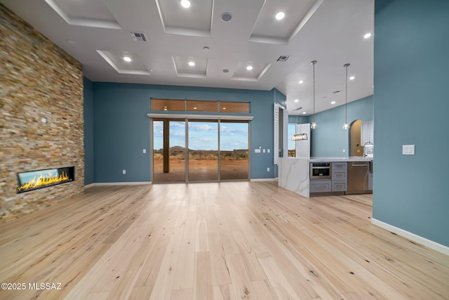 unfurnished living room with light wood-type flooring, a towering ceiling, and a fireplace