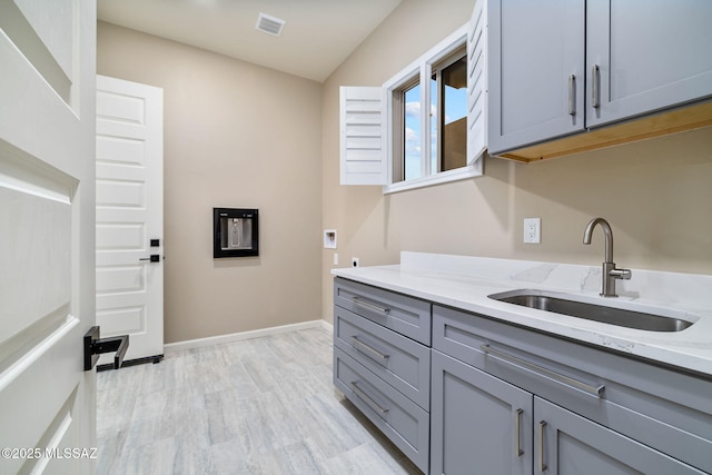 kitchen with sink, light wood-type flooring, gray cabinetry, and light stone countertops