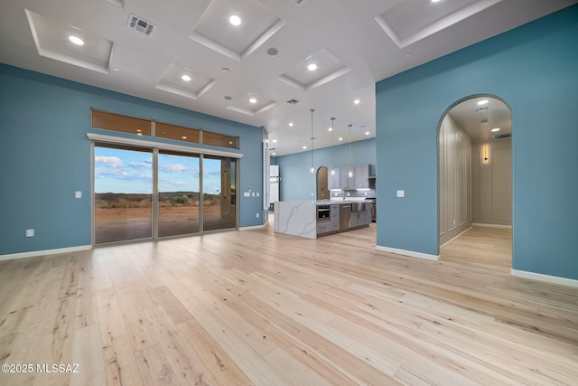 unfurnished living room featuring coffered ceiling, light hardwood / wood-style floors, and a towering ceiling